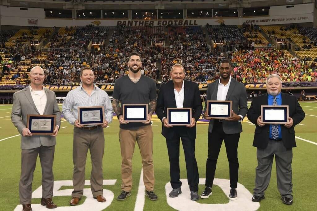six men in suits accepting awards on a football field